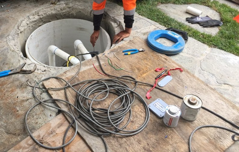Technician connecting pump wiring inside a septic riser